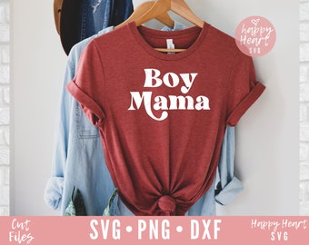 May include: A red t-shirt with the text "Boy Mama" in white retro-style lettering. The shirt is hanging on a wooden hanger.