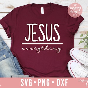 May include: A maroon t-shirt with the text "JESUS everything" in white lettering. The shirt is laid flat on a white wooden surface with a pair of white sneakers and a pair of blue jeans.