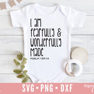 Op de afbeelding: Witte baby romper met zwarte tekst die "Ik ben ontzaglijk en wonderbaarlijk gemaakt PSALM 139:14" luidt.