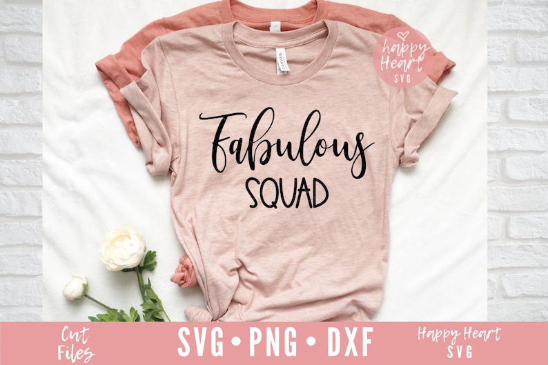 May include: A pink t-shirt with the text "fabulous squad" in black cursive lettering. The shirt is folded and laid on a white surface with a white flower.
