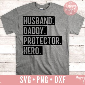 K&ouml;nnte beinhalten: Ein graues T-Shirt mit schwarzem Text, der "Husband. Daddy. Protector. Hero." lautet.
