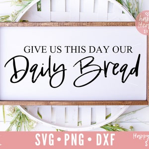 May include: A white wooden sign with a brown frame, featuring the text "GIVE US THIS DAY OUR Daily Bread" in black cursive font.