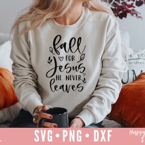 Puede incluir: Una sudadera blanca con el texto "fall for Jesus he never leaves" en letras negras. La sudadera la lleva puesta una persona sentada en un sofá con un cojín de calabaza.