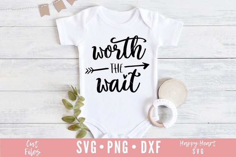 Op de afbeelding: Witte baby romper met zwarte tekst die "worth the wait" zegt met een pijl die naar rechts wijst. De romper ligt op een witte houten achtergrond.