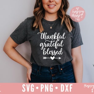 May include: A gray t-shirt with the text "thankful grateful blessed" in white cursive lettering. A white arrow with a small heart is below the text. The shirt is being worn by a person.