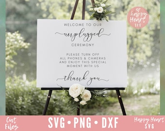 May include: White sign with black text that reads "Welcome to our unplugged ceremony. Please turn off all phones & cameras and enjoy this special moment with us. Thank you." The sign is on an easel with white flowers in front of it.
