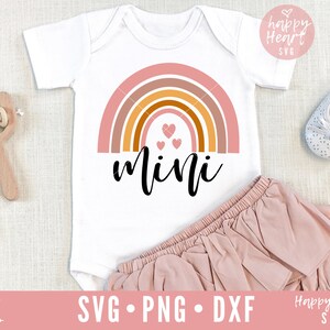 May include: A white onesie with a rainbow design and the word "mini" in black script. There are three small pink hearts in the center of the rainbow.