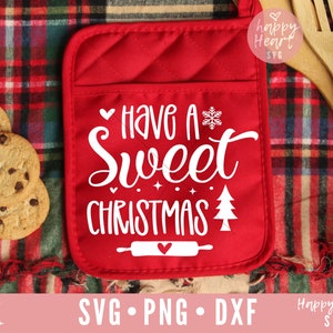 May include: Red oven mitt with the text "Have a Sweet Christmas" in white script. The mitt features a snowflake, Christmas tree, and rolling pin design. Chocolate chip cookies are on the left.
