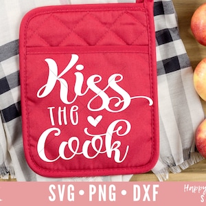 Pode incluir: Um pegador de panela acolchoado vermelho com o texto "Kiss the Cook" em letras brancas com um pequeno coração.