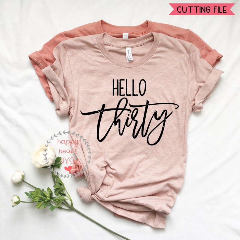May include: A pink t-shirt with the text "HELLO thirty" in black script font. The shirt is folded and laid flat on a white surface.