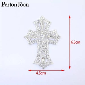 Może przedstawiać: Srebrna aplikacja w kształcie krzyża z kryształkami o szerokości 4,5 cm i wysokości 6,3 cm.