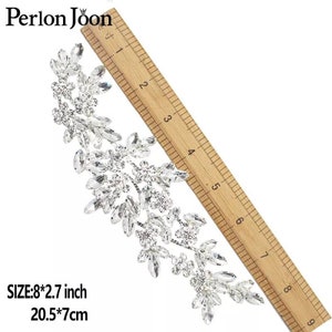 May include: A silver rhinestone embellishment measuring 8 inches by 2.7 inches, or 20.5 centimetres by 7 centimetres. The embellishment is shaped like a branch with leaves and flowers, all made of rhinestones.