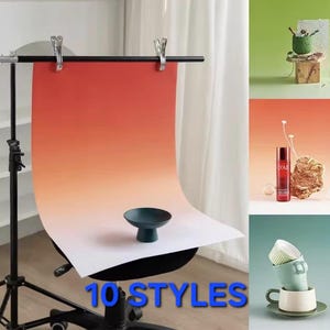 Może przedstawiać: Ustawienie fotograficzne z czerwono-pomarańczowym gradientowym tłem trzymanym przez czarny stojak. Mała, ciemnozielona miska stoi na papierze. Obraz pokazuje również trzy przykłady stylizacji produktów, w tym zielony obiekt, czerwoną butelkę i ułożone w stos filiżanki. Tekst brzmi "10 STYLES".