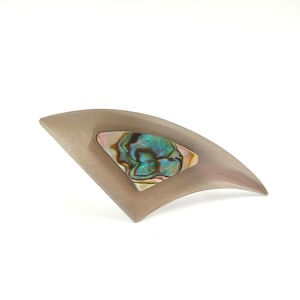 以下が含まれることがあります： アワビの貝殻をはめ込んだ、銀色の扇形のブローチ。虹色の貝殻は、緑、青、ピンクの色合いを見せています。ブローチは滑らかで光沢のある仕上がりで、ジャケットやスカーフに適した曲線的なデザインです。