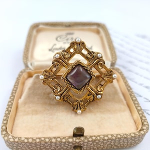 Vintage ornate brooch with simulated seed pearls and a purple diamond shaped stone antique gold colour metal scrolls flourishes renaissance