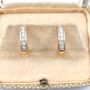 May include: A pair of gold hoop earrings with a row of clear diamonds set in the band.