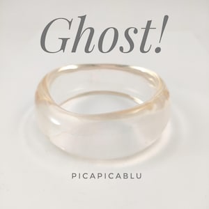May include: A clear, translucent resin ring with a smooth, rounded band. The word Ghost! is printed in large grey letters above the ring, and the text PICAPICABLU is printed in smaller grey letters below the ring.