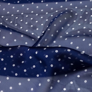 Può includere: Un tessuto leggero e trasparente caratterizzato da un colore di base blu navy profondo con un motivo ripetitivo di piccoli pois bianchi solidi. Il materiale è drappeggiato in morbide pieghe, creando vari livelli di trasparenza.