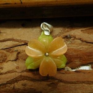 Puede incluir: Un colgante de flor de color melocot&oacute;n tallado en piedra con detalles verdes. El colgante tiene una anilla de plata.