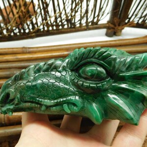 Puede incluir: Una escultura de cabeza de drag&oacute;n de jade verde con detalles intrincados. El ojo del drag&oacute;n est&aacute; tallado con un aspecto realista. La escultura est&aacute; hecha de jade pulido y tiene un acabado liso y brillante.