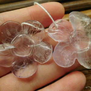 May include: Two pale pink flower-shaped crystal pendants with a white string attached.