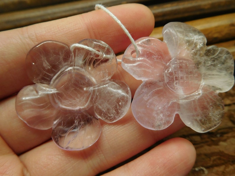 May include: Two pale pink flower-shaped crystal pendants with a white string attached.