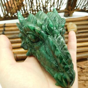 Puede incluir: Escultura de cabeza de drag&oacute;n verde tallada en jade. El drag&oacute;n tiene escamas detalladas y una expresi&oacute;n feroz.