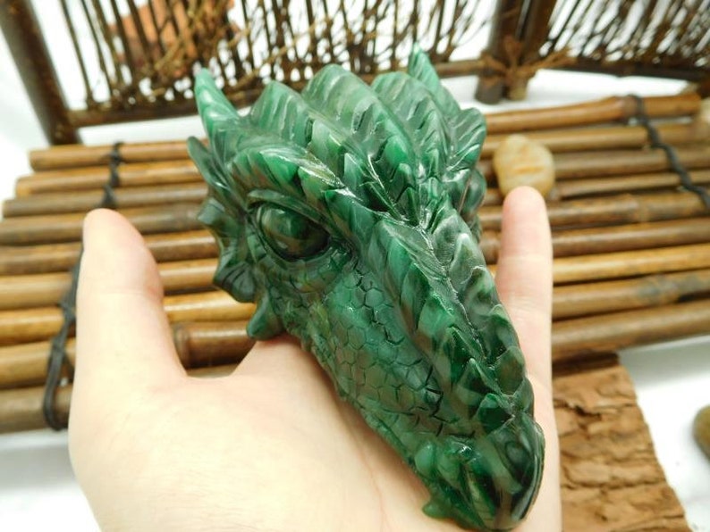 Puede incluir: Escultura de cabeza de drag&oacute;n verde tallada en jade. El drag&oacute;n tiene escamas detalladas y una expresi&oacute;n feroz.