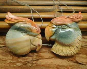 May include: Two carved parrot pendants made of colorful agate stone. The parrots are facing different directions and have detailed carvings of feathers and beaks.