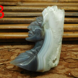Puede incluir: Una escultura de piedra de &aacute;gata tallada de una cara, con un patr&oacute;n de bandas blancas y grises. La escultura est&aacute; sobre una superficie de madera marr&oacute;n.
