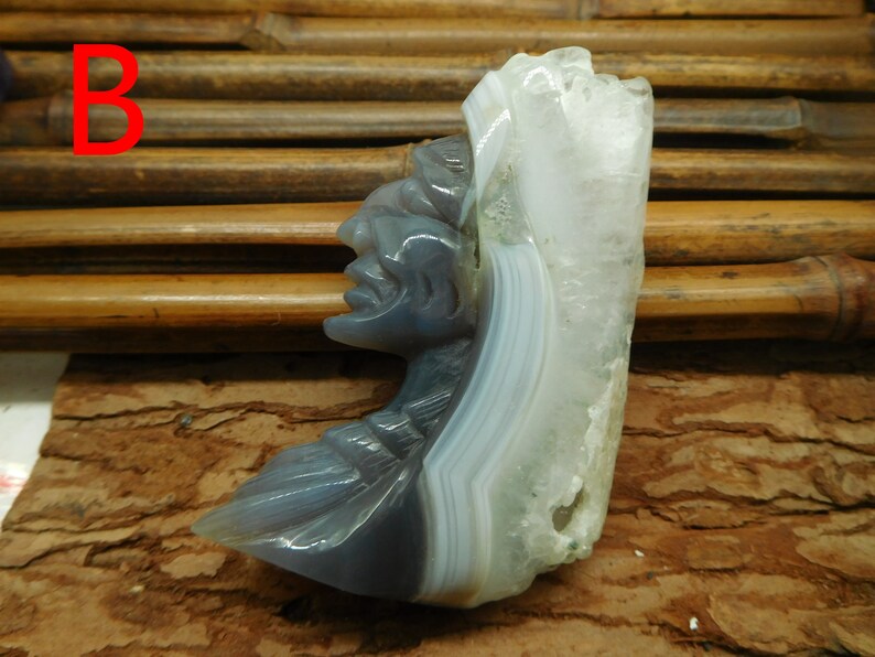 Puede incluir: Una escultura de piedra de &aacute;gata tallada de una cara, con un patr&oacute;n de bandas blancas y grises. La escultura est&aacute; sobre una superficie de madera marr&oacute;n.