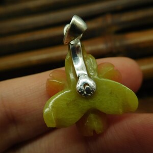 Puede incluir: Un colgante de jade verde y amarillo en forma de flor con una anilla de plata. El colgante est&aacute; tallado en forma de flor con cinco p&eacute;talos.
