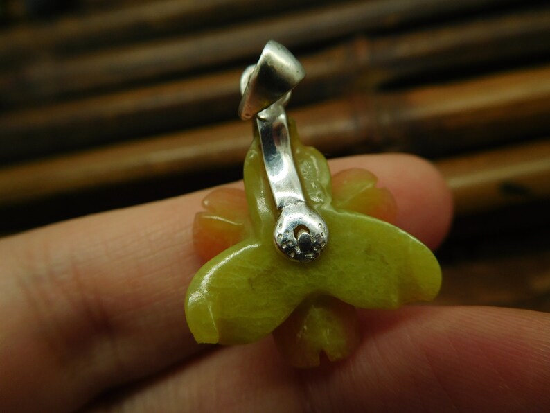 Puede incluir: Un colgante de jade verde y amarillo en forma de flor con una anilla de plata. El colgante est&aacute; tallado en forma de flor con cinco p&eacute;talos.