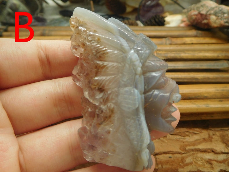 Puede incluir: Una escultura tallada en piedra de &aacute;gata de un jefe nativo americano con un tocado de plumas. La piedra es de color gris claro con marcas marrones y blancas.