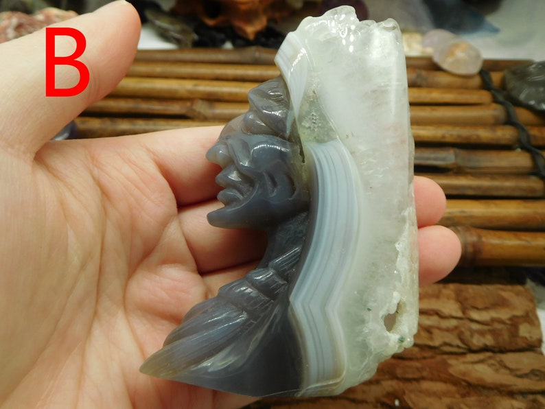 Puede incluir: Una escultura tallada en piedra de &aacute;gata de la cabeza de un jefe nativo americano, con un cristal de &aacute;gata blanco en la parte superior. La escultura es gris y blanca con una talla detallada de la cara.