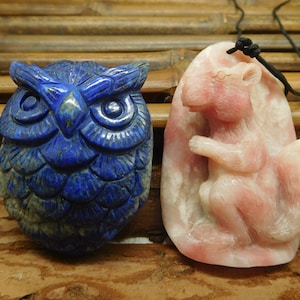 Puede incluir: Dos colgantes de piedra tallada, uno un búho azul y el otro una ardilla rosa.