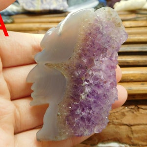 Puede incluir: Un colgante de amatista tallado con un dise&ntilde;o de perfil de rostro. La amatista es de color morado oscuro y tiene una textura natural y rugosa. El colgante mide aproximadamente 5 cm de alto.