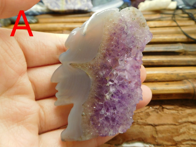 Puede incluir: Un colgante de amatista tallado con un dise&ntilde;o de perfil de rostro. La amatista es de color morado oscuro y tiene una textura natural y rugosa. El colgante mide aproximadamente 5 cm de alto.