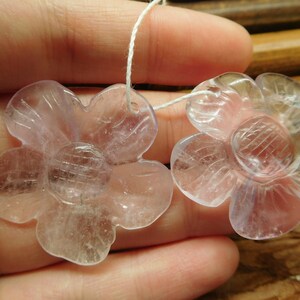 May include: Two clear, pale lavender flower-shaped crystal beads with a hole for stringing.