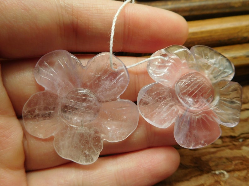 May include: Two clear, pale lavender flower-shaped crystal beads with a hole for stringing.