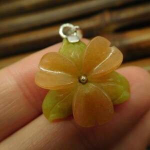 Puede incluir: Un delicado colgante de flor hecho de piedra verde y naranja tallada. El colgante tiene un aro de plata y una peque&ntilde;a perla de plata en el centro.