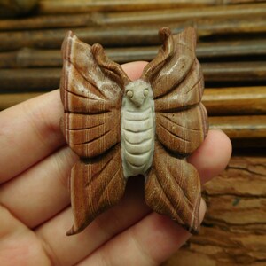 May include: A carved wooden butterfly with brown and white stripes. The butterfly is intricately detailed and has a realistic appearance.