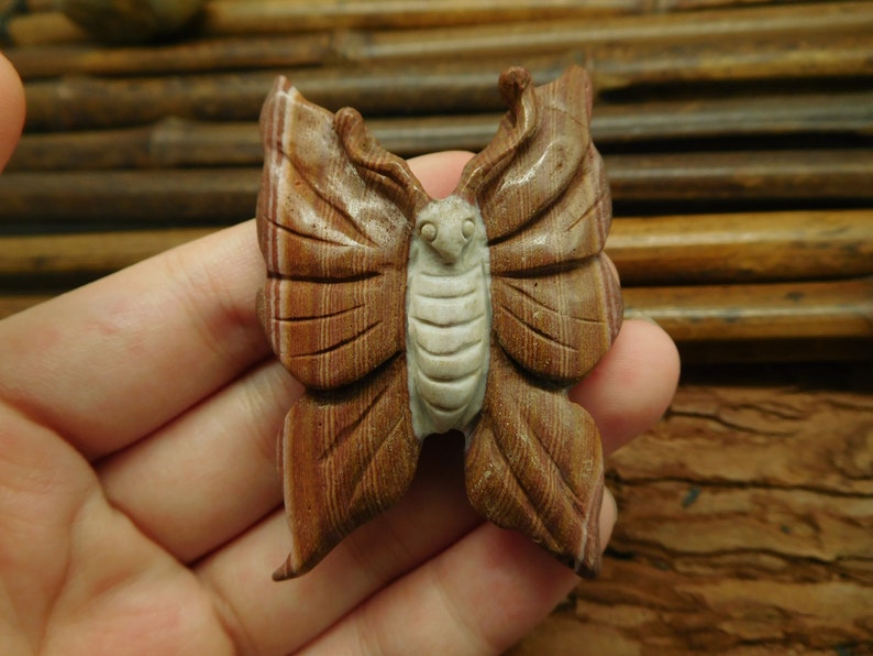 May include: A carved wooden butterfly with brown and white stripes. The butterfly is intricately detailed and has a realistic appearance.