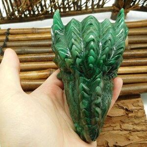 Puede incluir: Escultura de cabeza de drag&oacute;n verde tallada en piedra. El drag&oacute;n tiene escamas detalladas y una expresi&oacute;n feroz.