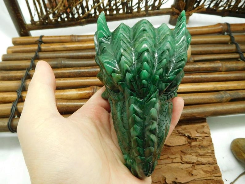 Puede incluir: Escultura de cabeza de drag&oacute;n verde tallada en piedra. El drag&oacute;n tiene escamas detalladas y una expresi&oacute;n feroz.