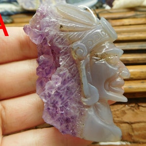 Puede incluir: Un colgante tallado en amatista y &aacute;gata con un perfil detallado de una cara con un tocado. El colgante es de color morado claro y gris.