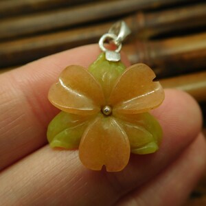 Puede incluir: Un colgante de flor tallada en piedra naranja y verde con un aro de plata.