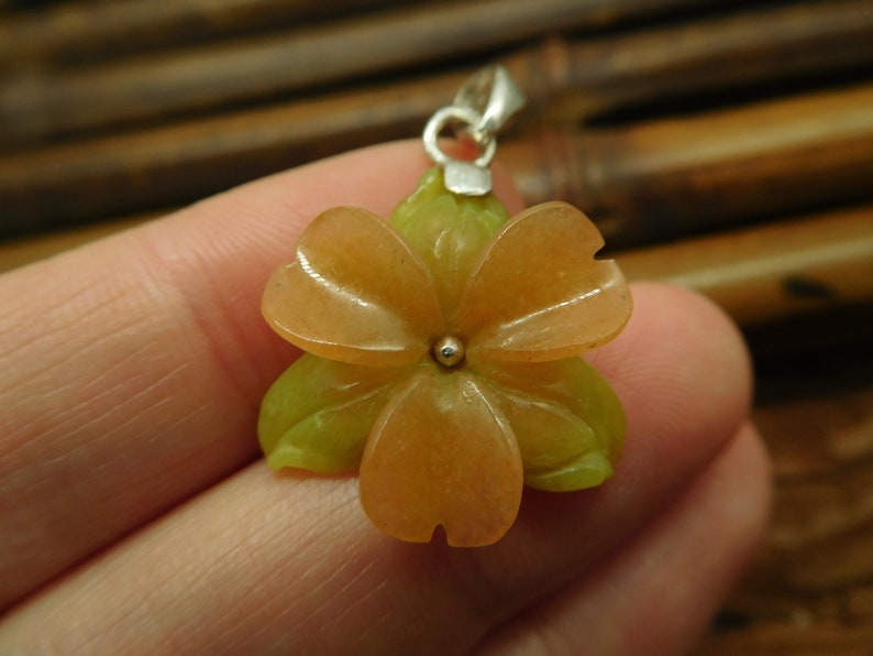 Puede incluir: Un colgante de flor tallada en piedra naranja y verde con un aro de plata.