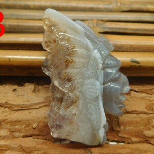 Puede incluir: Una escultura de piedra tallada de una cara con detalles intrincados. La escultura est&aacute; hecha de una piedra gris clara con acentos marrones y blancos. La escultura est&aacute; sentada sobre una superficie de madera.