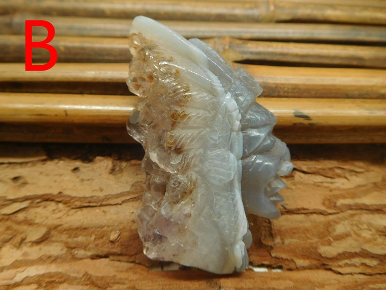 Puede incluir: Una escultura de piedra tallada de una cara con detalles intrincados. La escultura est&aacute; hecha de una piedra gris clara con acentos marrones y blancos. La escultura est&aacute; sentada sobre una superficie de madera.